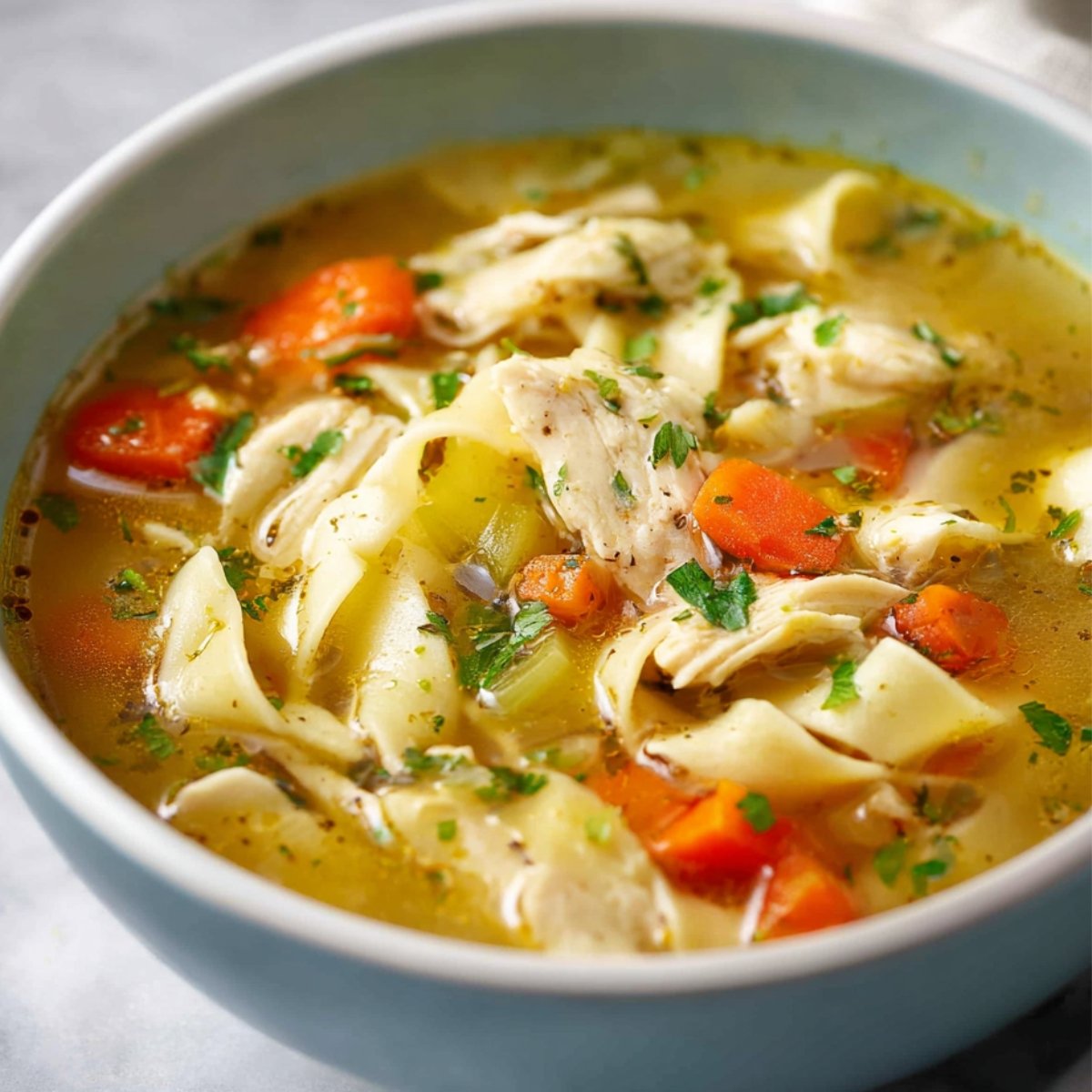 Chicken Noodle Soup Bowl of homemade chicken noodle soup with shredded chicken, egg noodles, carrots, celery, and herbs in golden broth