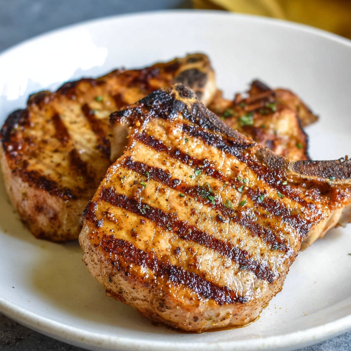 Pork Chop Marinade A plate with two golden, grilled pork chops that have perfect grill marks. The pork is tender and juicy, topped with a light seasoning, ready to be served with a side dish.