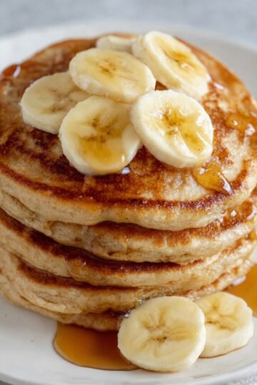 banana pancakes A stack of fluffy banana pancakes topped with sliced bananas and drizzled with syrup, ready to be enjoyed as a delicious breakfast.