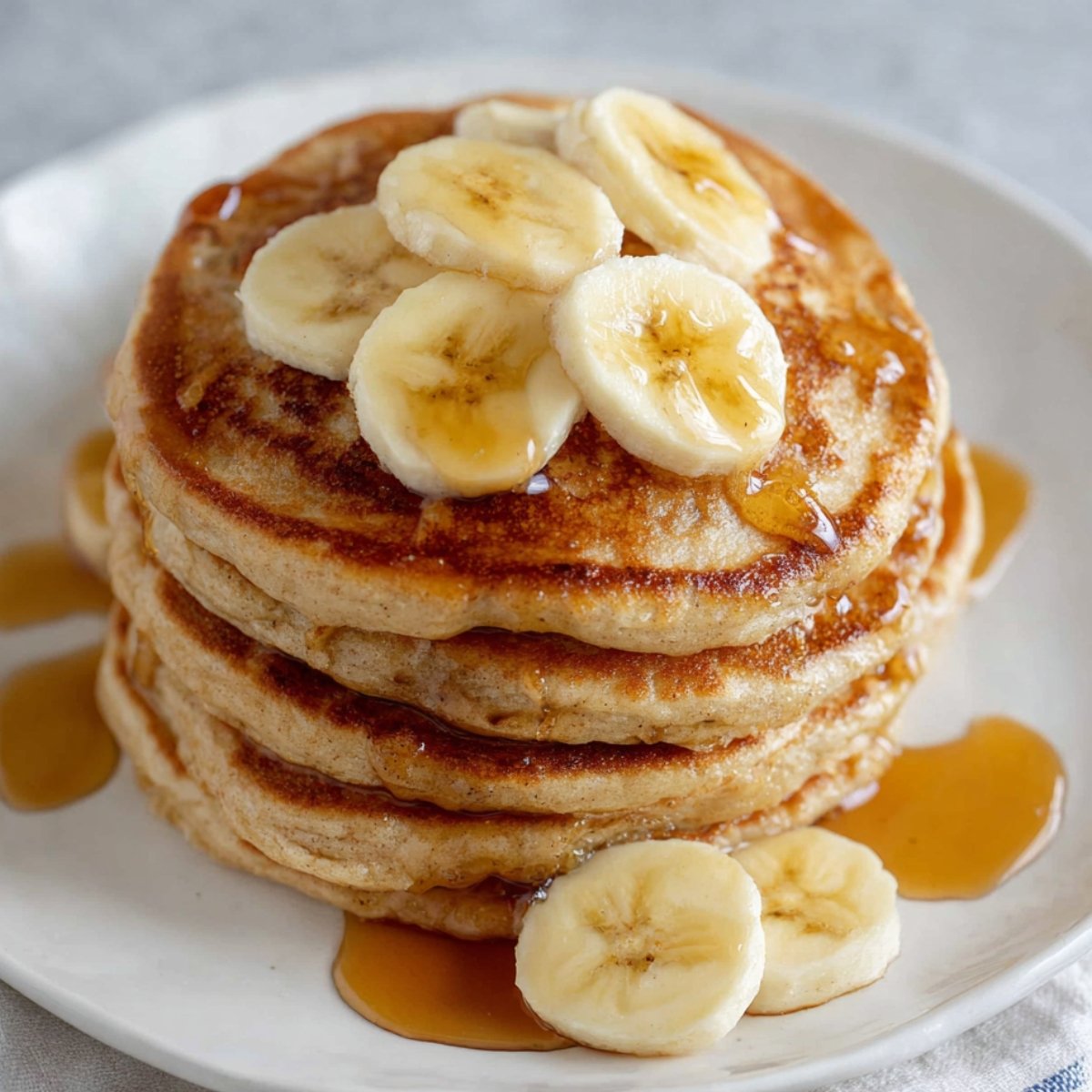banana pancakes A stack of fluffy banana pancakes topped with sliced bananas and drizzled with syrup, ready to be enjoyed as a delicious breakfast.