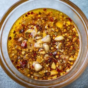 A bowl of aromatic marinade filled with finely chopped garlic, spices, and oil, creating a vibrant and flavorful blend. The mixture has a warm, golden hue, promising a zesty kick for the pork chops.