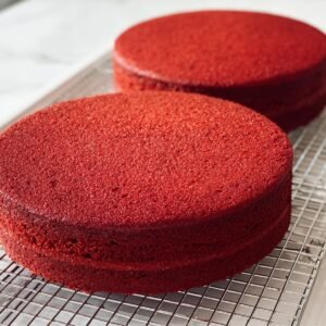 “Two round red velvet strawberry cake layers cooling on a metal wire rack in a bright white kitchen.”