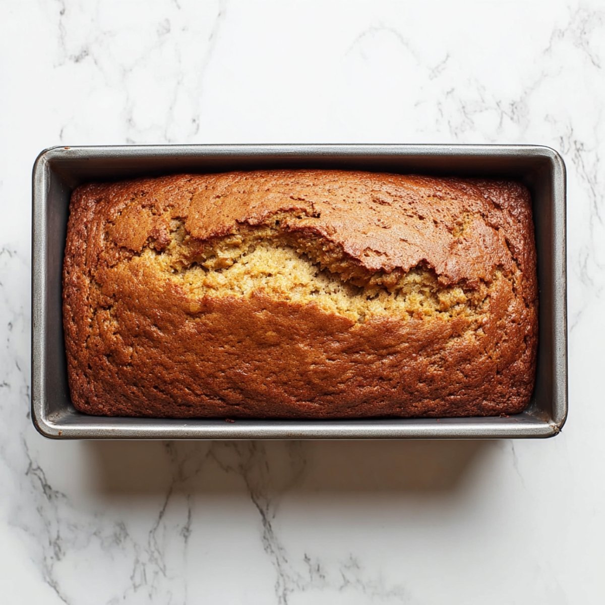 Sliced banana bread with a moist, soft crumb on a wooden cutting board, bananas in the background.