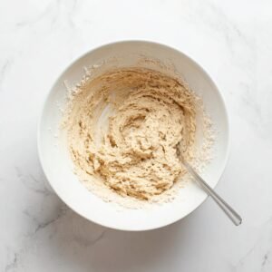 Banana bread batter being mixed in a white bowl on a marble countertop.