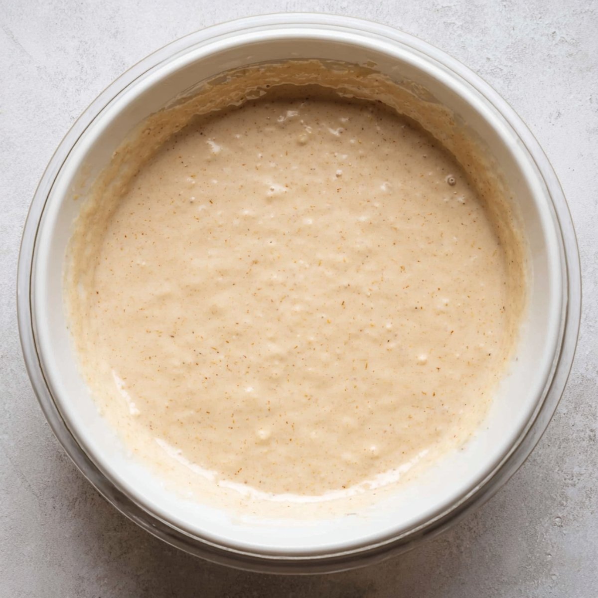 A glass bowl filled with pancake batter. The batter has a smooth, creamy consistency with small air bubbles, ready to be poured onto a griddle