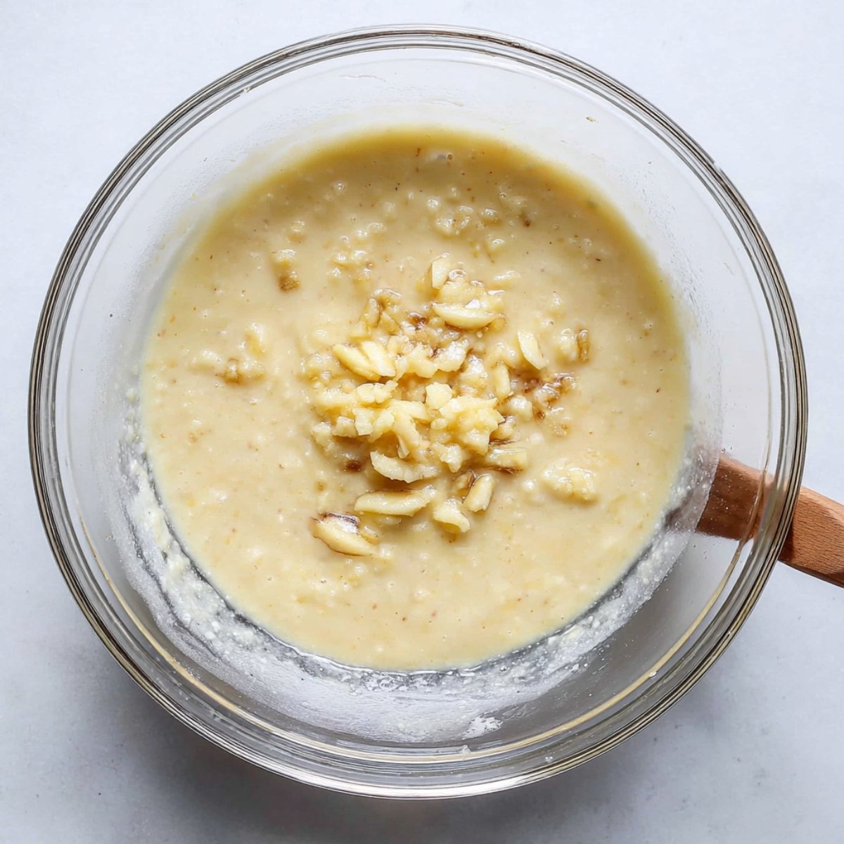 Banana pancake batter in a bowl, with small lumps of banana pieces. The batter is thick and ready to be cooked into pancakes.