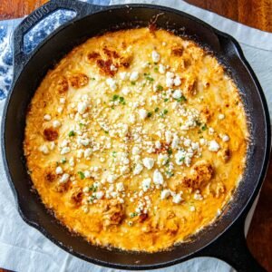 Overhead view of creamy buffalo chicken dip baked in a cast iron skillet and topped with crumbled blue cheese.