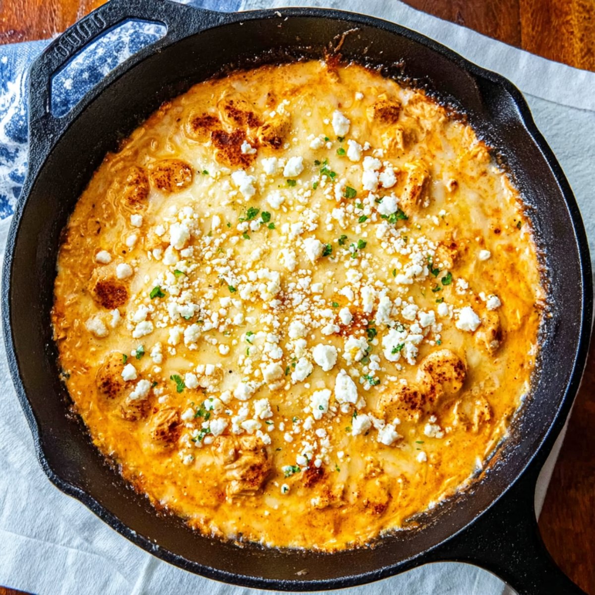 Overhead view of creamy buffalo chicken dip baked in a cast iron skillet and topped with crumbled blue cheese.