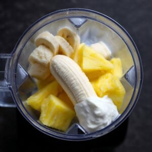 Frozen pineapple chunks, a banana, and Greek yogurt inside a blender, ready to be blended into a tropical smoothie.