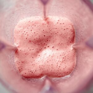 A blender containing crushed strawberries and powder, possibly with additional ingredients being added for blending.