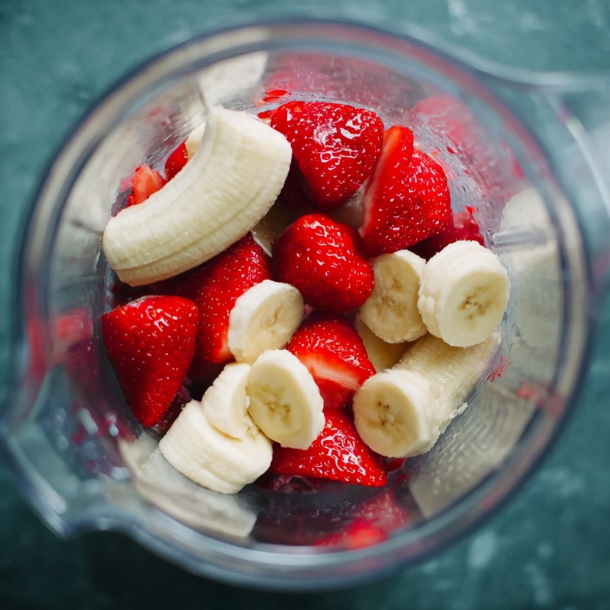 A blender filled with chopped bananas and strawberries, ready to be blended into a smoothie.