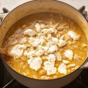 A large pot of white chicken chili with cream cheese cubes floating on top, ready to be stirred in