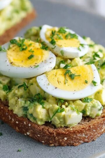 Avocado Egg Salad A creamy avocado egg salad served on toasted whole grain bread, garnished with slices of hard-boiled egg and fresh herbs, showcasing a healthy and flavorful meal.