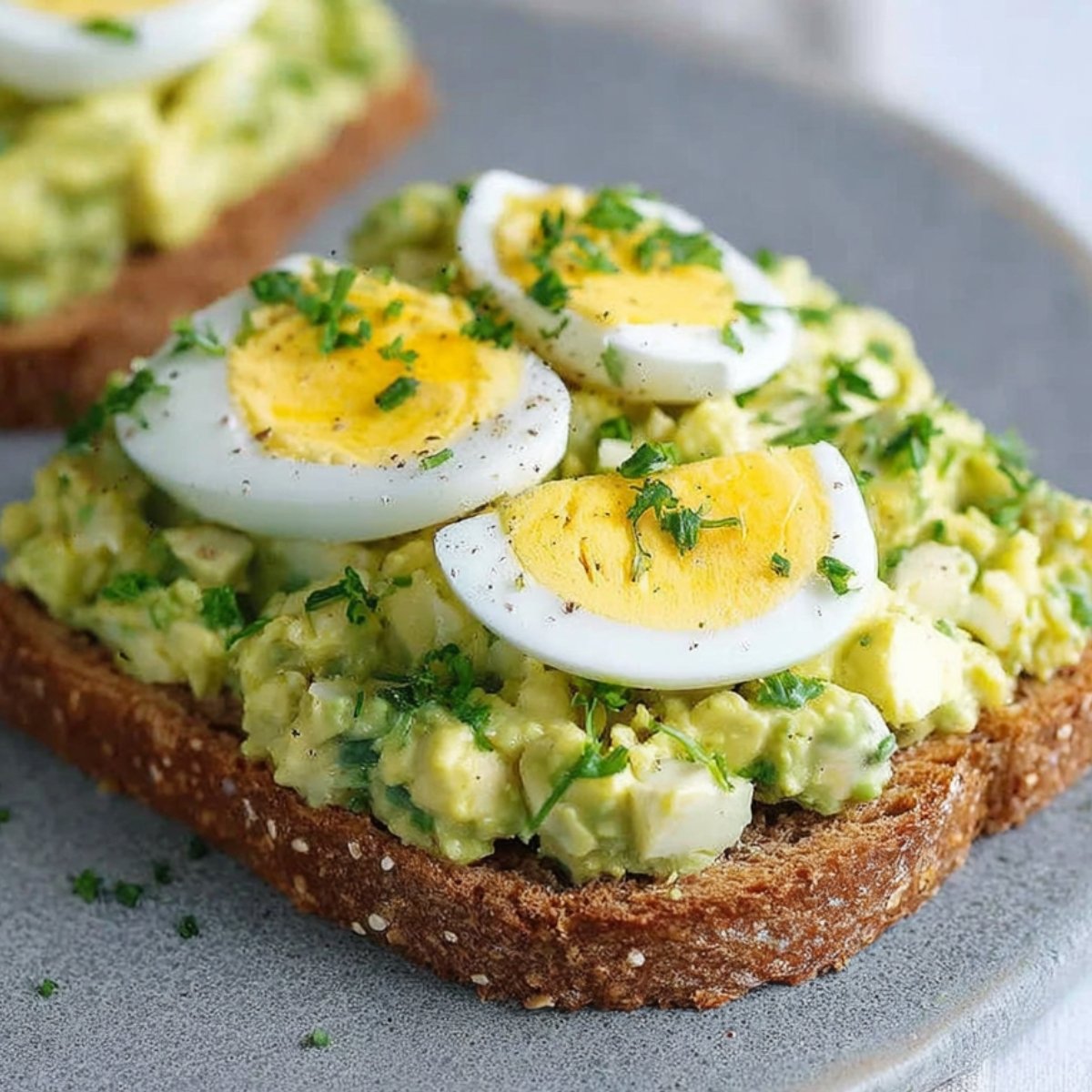 Avocado Egg Salad A creamy avocado egg salad served on toasted whole grain bread, garnished with slices of hard-boiled egg and fresh herbs, showcasing a healthy and flavorful meal.
