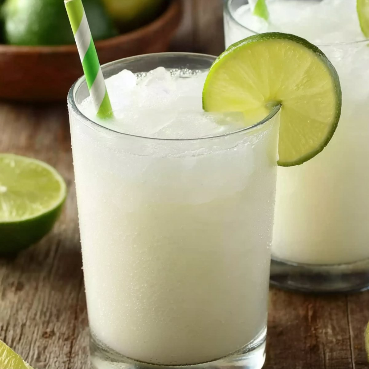 Brazilian Lemonade Two refreshing glasses of Brazilian lemonade with a straw, garnished with lime wedges, on a wooden surface.