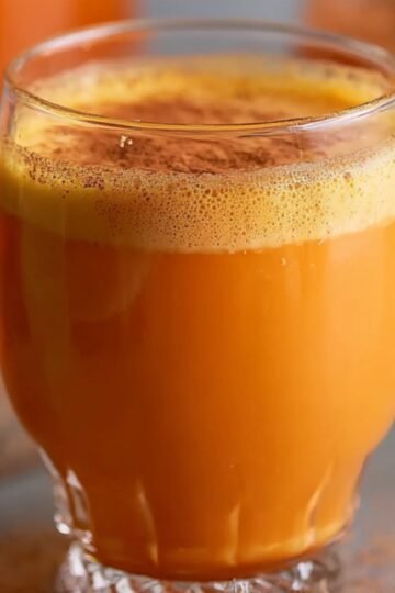 Carrot Juice Recipe A glass of freshly made Caribbean carrot juice topped with a sprinkle of cinnamon, creating a warm and inviting look. The orange juice contrasts beautifully with the cinnamon dust, and the jar of juice is visible in the background.
