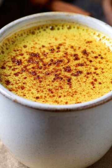 Golden Milk Recipe A cozy cup of golden milk, sprinkled with cinnamon on top, served in a white mug.