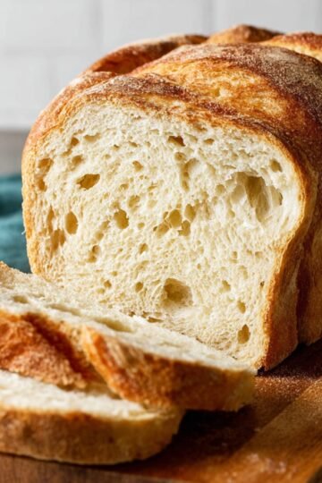 Sourdough Bread A freshly baked loaf of bread is sliced, showing a soft and airy crumb with large air pockets inside.