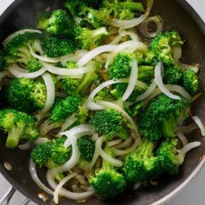 Pieces of beef cooking in a pan with a cornstarch coating, giving the beef a glossy, tender appearance. The beef is browning and cooking in a small amount of sauce, with a clean kitchen backdrop