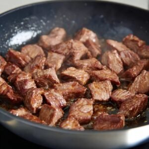 A pan of fresh broccoli and sliced onions sautéing together, with the broccoli remaining bright green and the onions soft and translucent. The ingredients are lightly coated in oil, with a simple kitchen background.