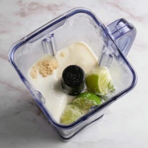 All the ingredients for Brazilian lemonade, including lime, condensed milk, and water, being added to a blender.