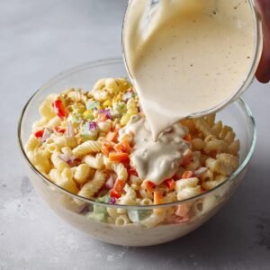 Pouring a creamy dressing over a fresh macaroni salad, ensuring every bite will be coated with a flavorful mixture