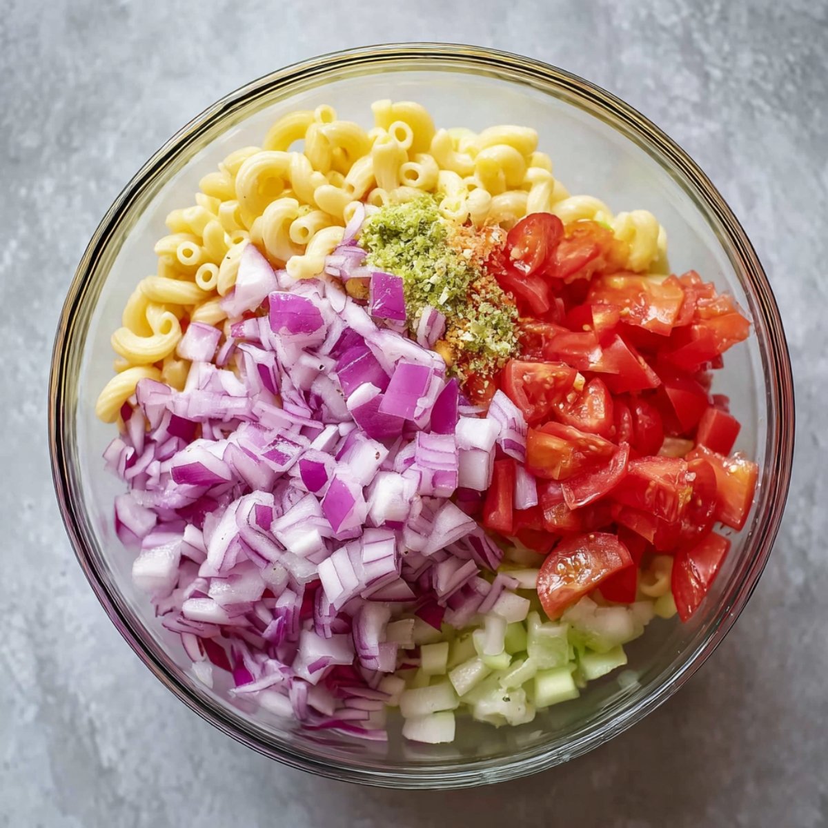 Chopped red onions, tomatoes, and other fresh vegetables are added to a bowl of macaroni, bringing color and texture to the dish.
