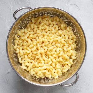 Strained cooked macaroni in a colander, ready to be mixed with fresh vegetables and a flavorful dressing for a perfect salad