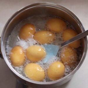 A pot filled with boiling water and several eggs being gently stirred with a blue spatula, showing the process of hard-boiling eggs for an avocado egg salad