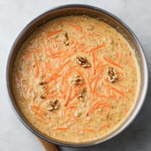 "A pan filled with creamy carrot cake batter, featuring fresh grated carrots and walnuts, ready to be baked into a delicious, moist treat."