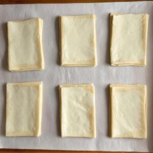 "Place the cut puff pastry squares on a baking sheet lined with parchment paper, making sure they are evenly spaced for even baking. These squares are the perfect base for your creamy cheese filling. The puff pastry will rise beautifully during baking, forming a golden, flaky crust that pairs wonderfully with the rich cheese center."