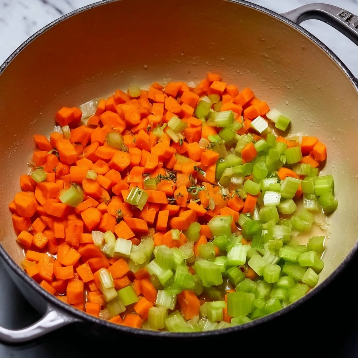 A pan with diced carrots and celery sautéing together, with hints of thyme, for a comforting chicken noodle soup base.