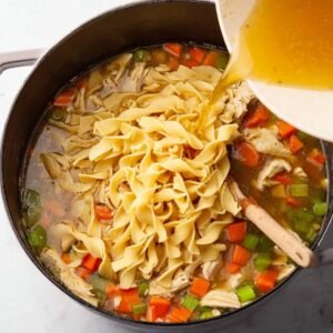 A wide shot of chicken noodle soup being stirred, with chunks of chicken, vegetables, and noodles in a flavorful broth.
