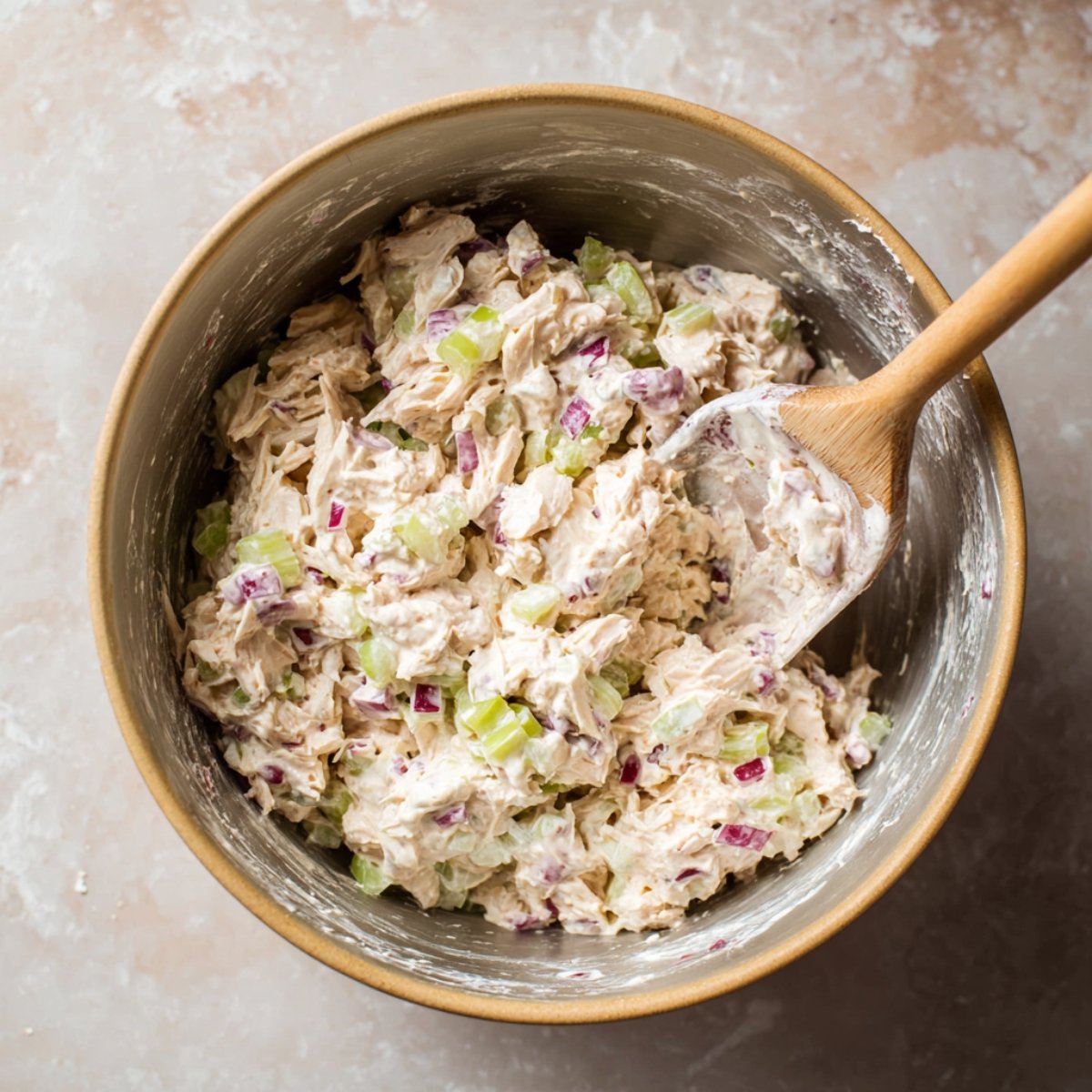 A creamy chicken salad with chunks of chicken, diced celery, and red onion mixed together in a bowl, ready to be served.