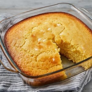 A glass dish of cornbread that’s just out of the oven, with a golden-brown crust and a light, fluffy interior. It’s the perfect homemade comfort food.