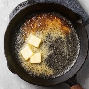 Pouring the prepared pancake batter into a hot, buttered cast iron skillet, ready to bake into a fluffy, golden pancake.