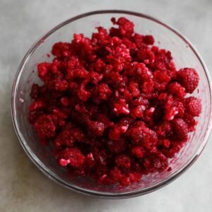 A bowl filled with chopped raspberries, showing their vivid red color and juicy texture, ready to be added to a recipe or dessert.