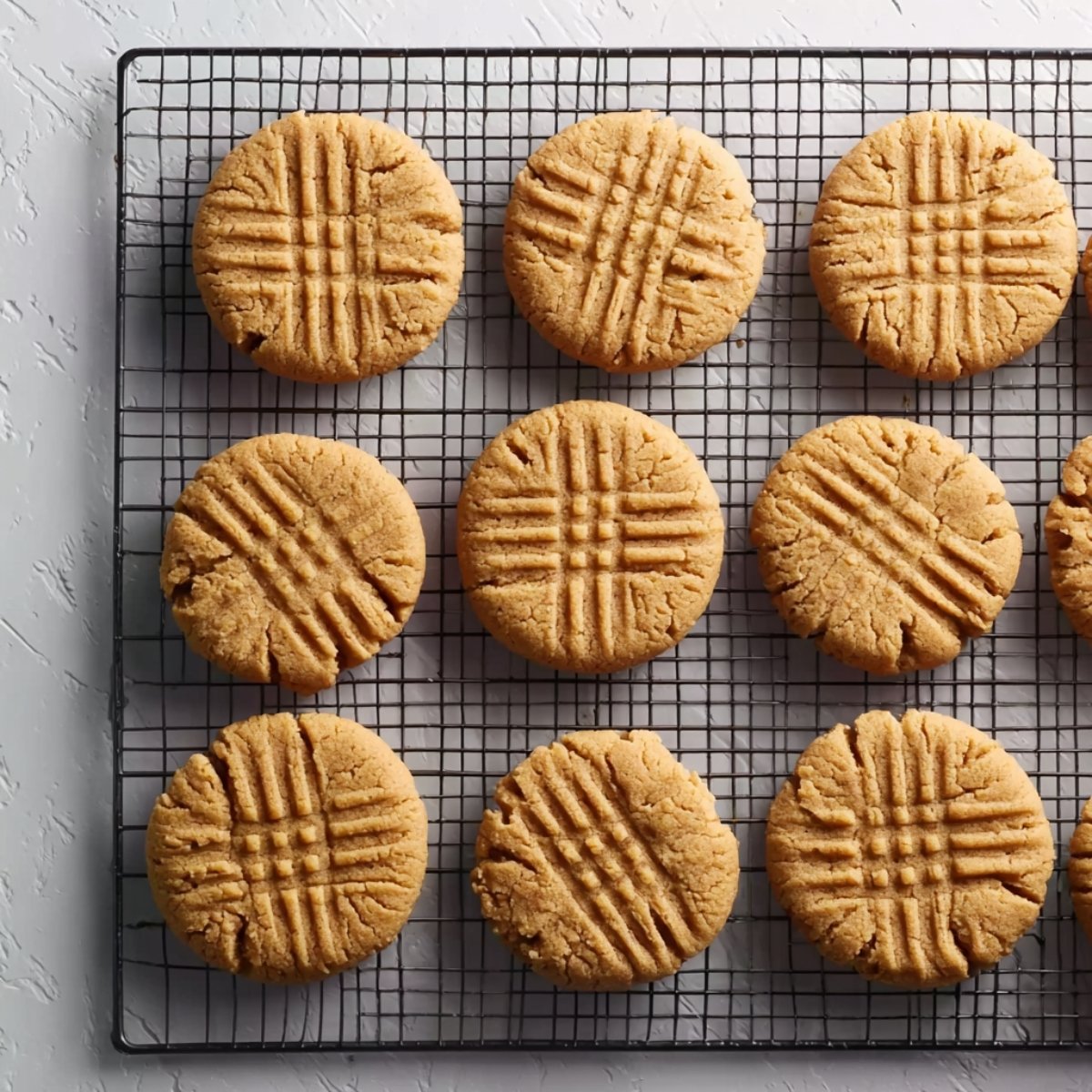 Peanut butter cookies with crisscross fork marks cooling on a black wire rack, photographed from above.