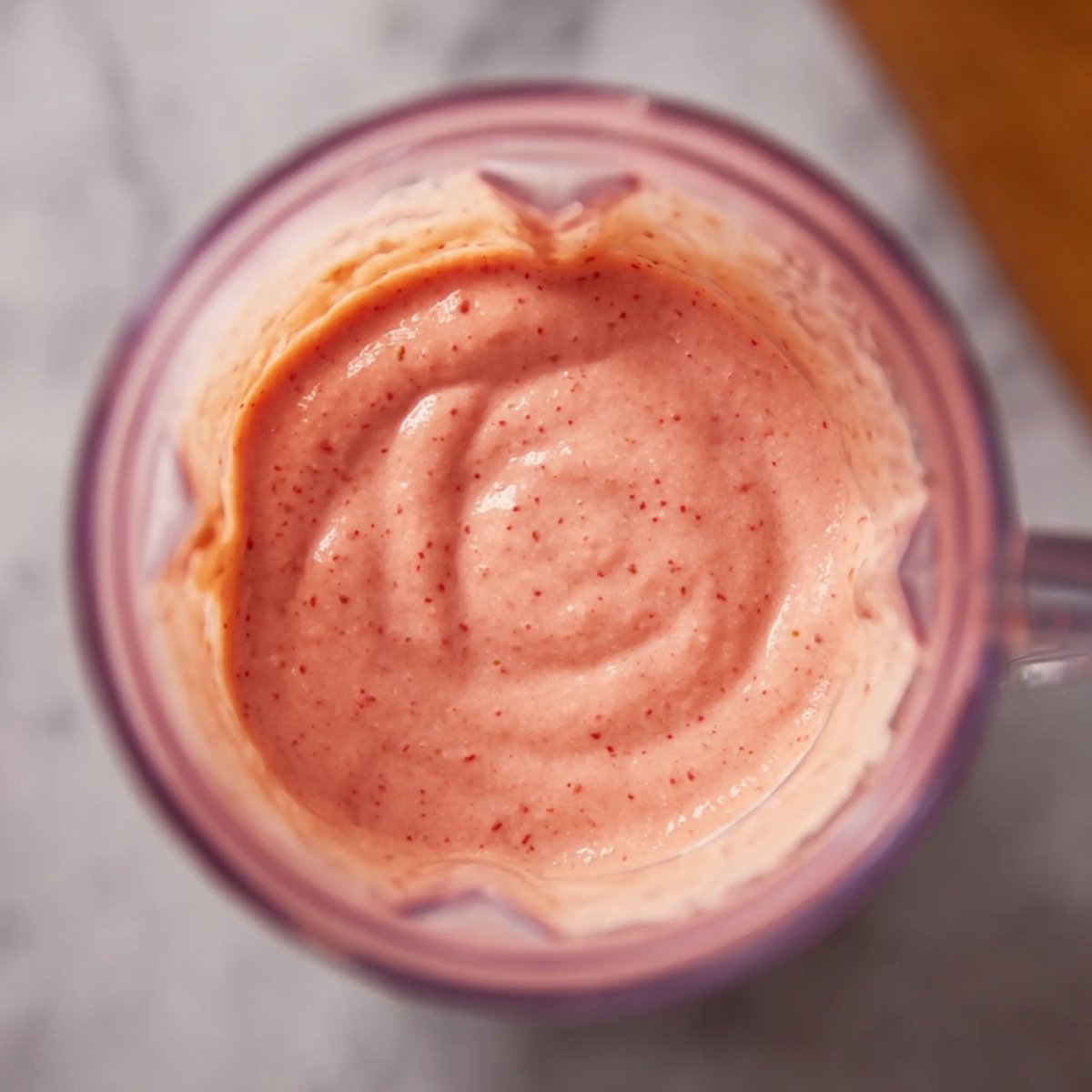 A close-up shot of a creamy, blended strawberry mango smoothie in a blender, showing its smooth and rich texture.