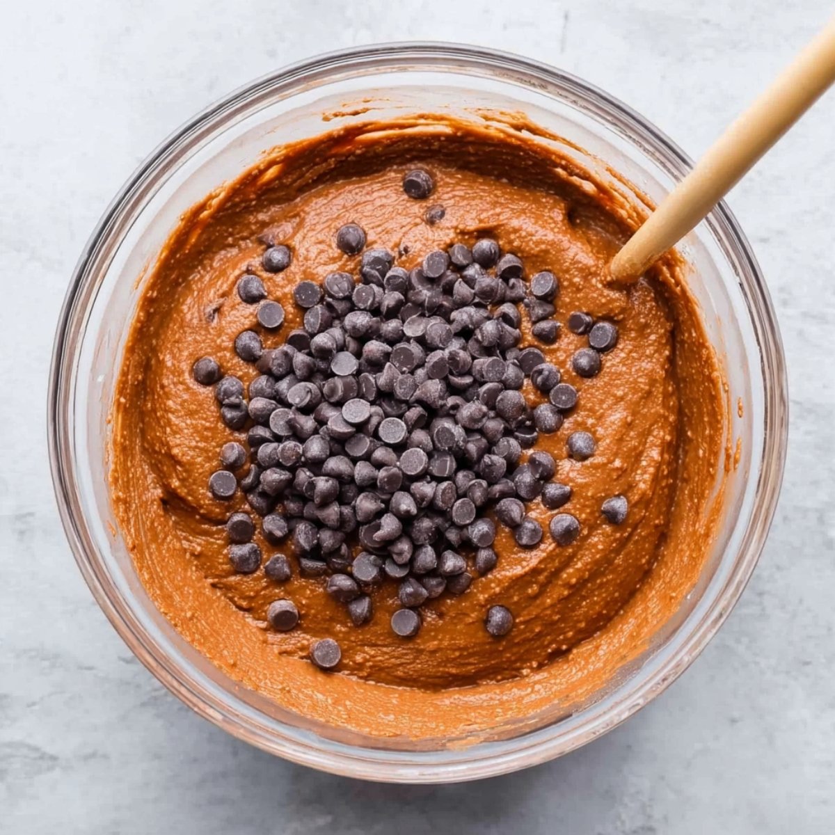 "A bowl of rich, smooth sweet potato brownie batter with chocolate chips ready to be folded in, offering a sneak peek of the decadent texture.