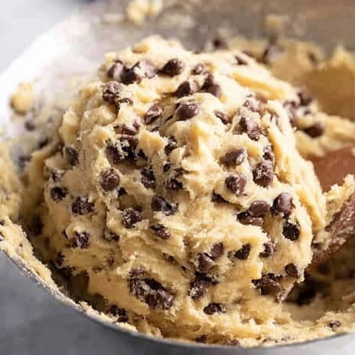 Close-up of a mixing bowl filled with thick chocolate chip cookie dough, generously studded with semi-sweet chocolate chips, ready to be scooped and baked.