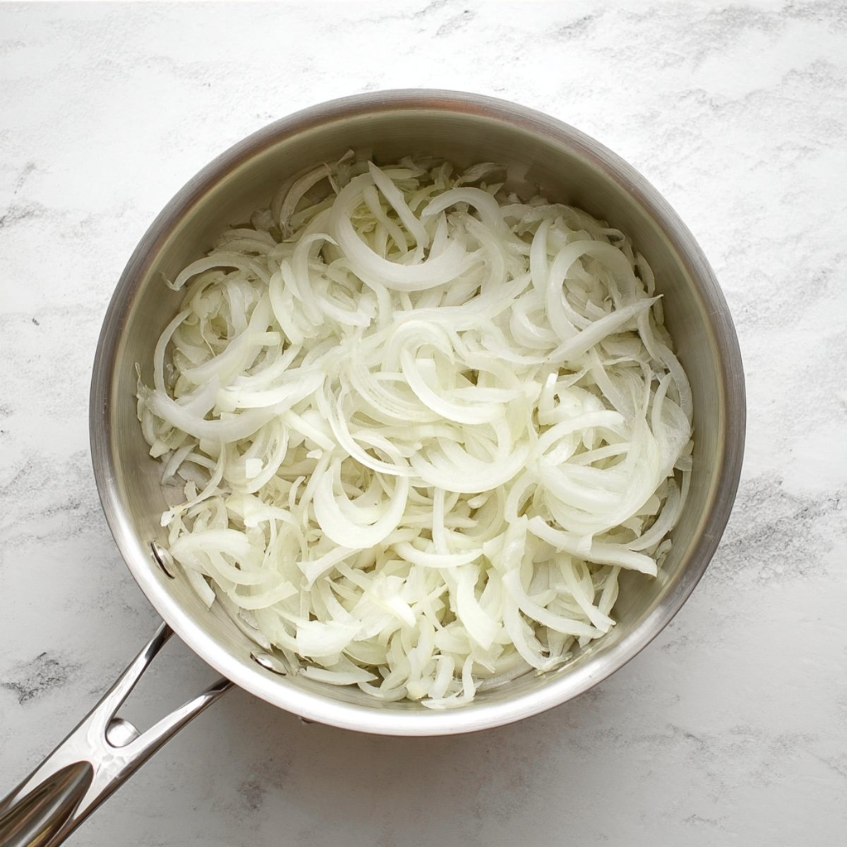 A pan filled with thinly sliced onions cooking on a stovetop.