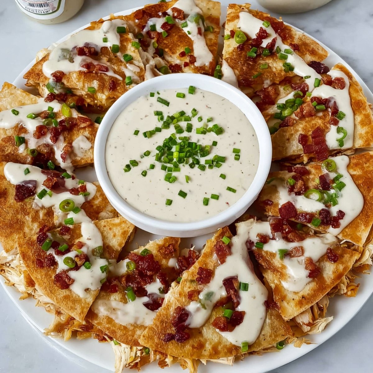 Crispy Chicken Bacon Ranch Quesadillas slices arranged around a bowl of creamy ranch dipping sauce, topped with crumbled bacon and fresh green onions. A delicious cheesy appetizer and easy party snack idea perfect for quick meals or game day food.
