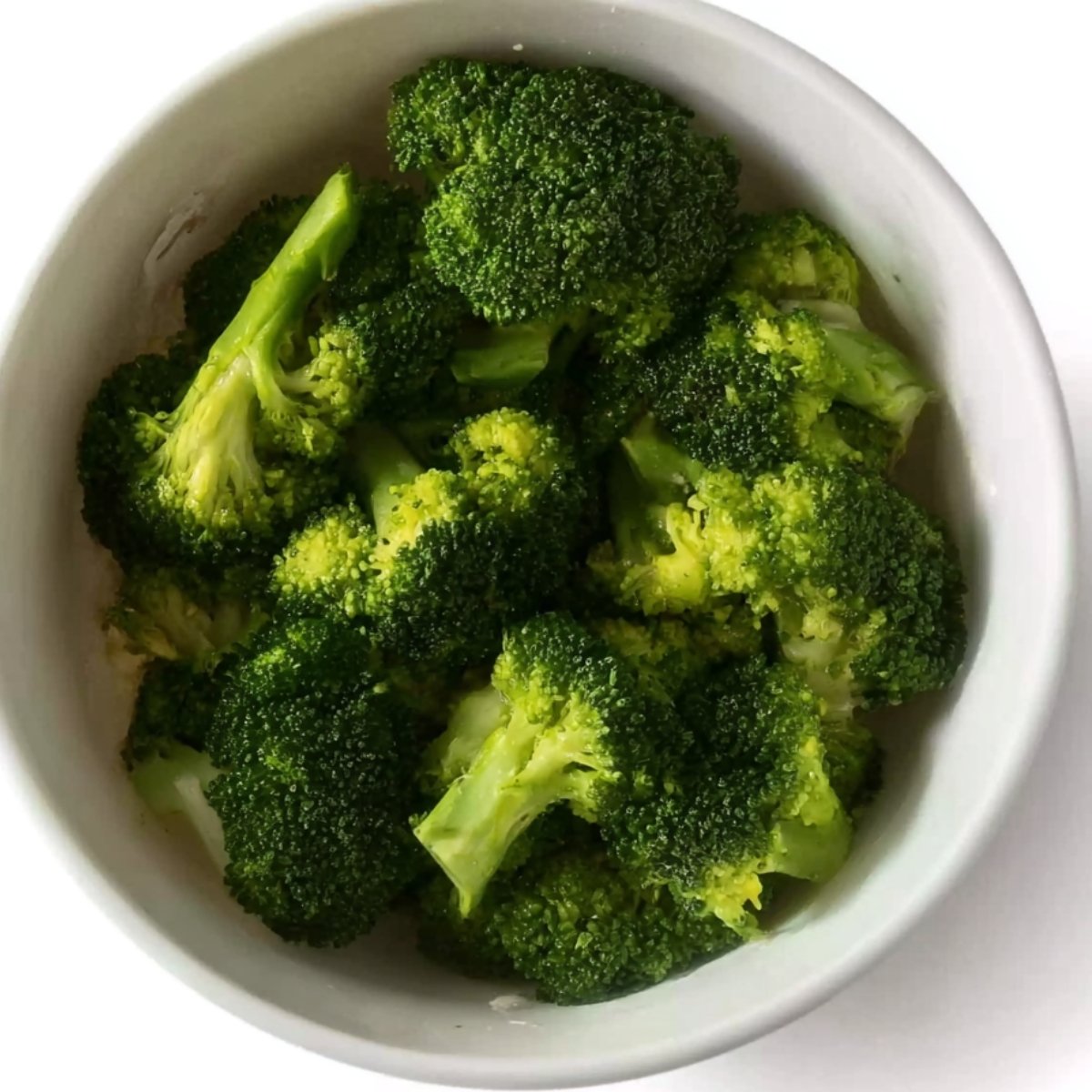 A bowl filled with cooked broccoli florets, vibrant green in color, prepared and ready to be used for a recipe.