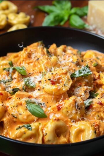 A mixture of shredded chicken, tortellini, and tomato sauce inside a slow cooker, cooking together for a hearty meal.