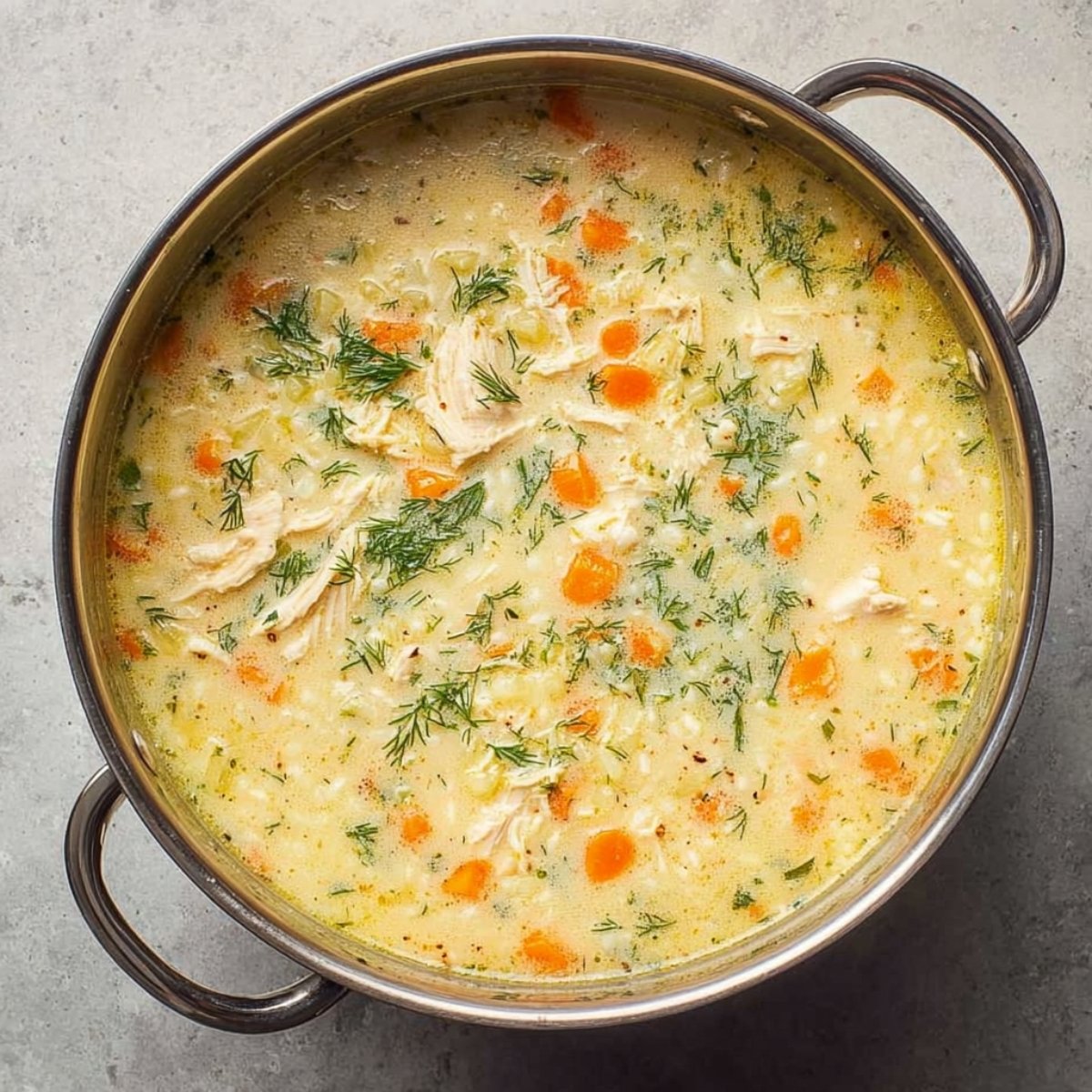 A pot of Greek lemon chicken soup being stirred, showing a creamy broth with diced carrots, celery, chicken pieces, and fresh herbs, ready to serve.