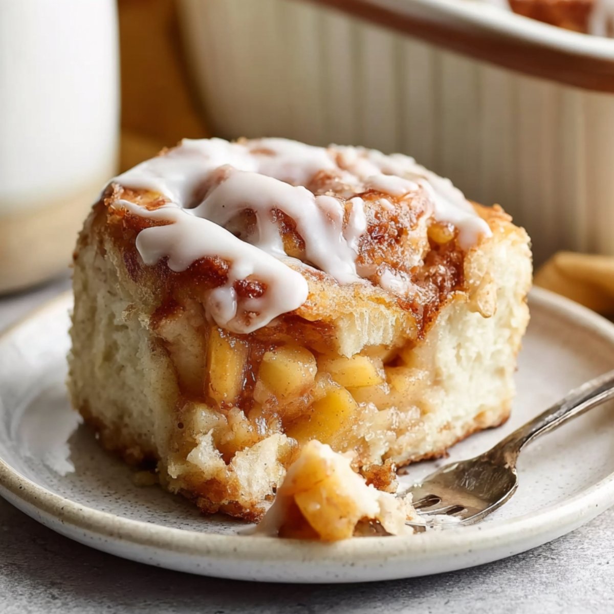 A baked Peach Cobbler Cinnamon Rolls topped with white icing on a plate, with a fork cutting into it.