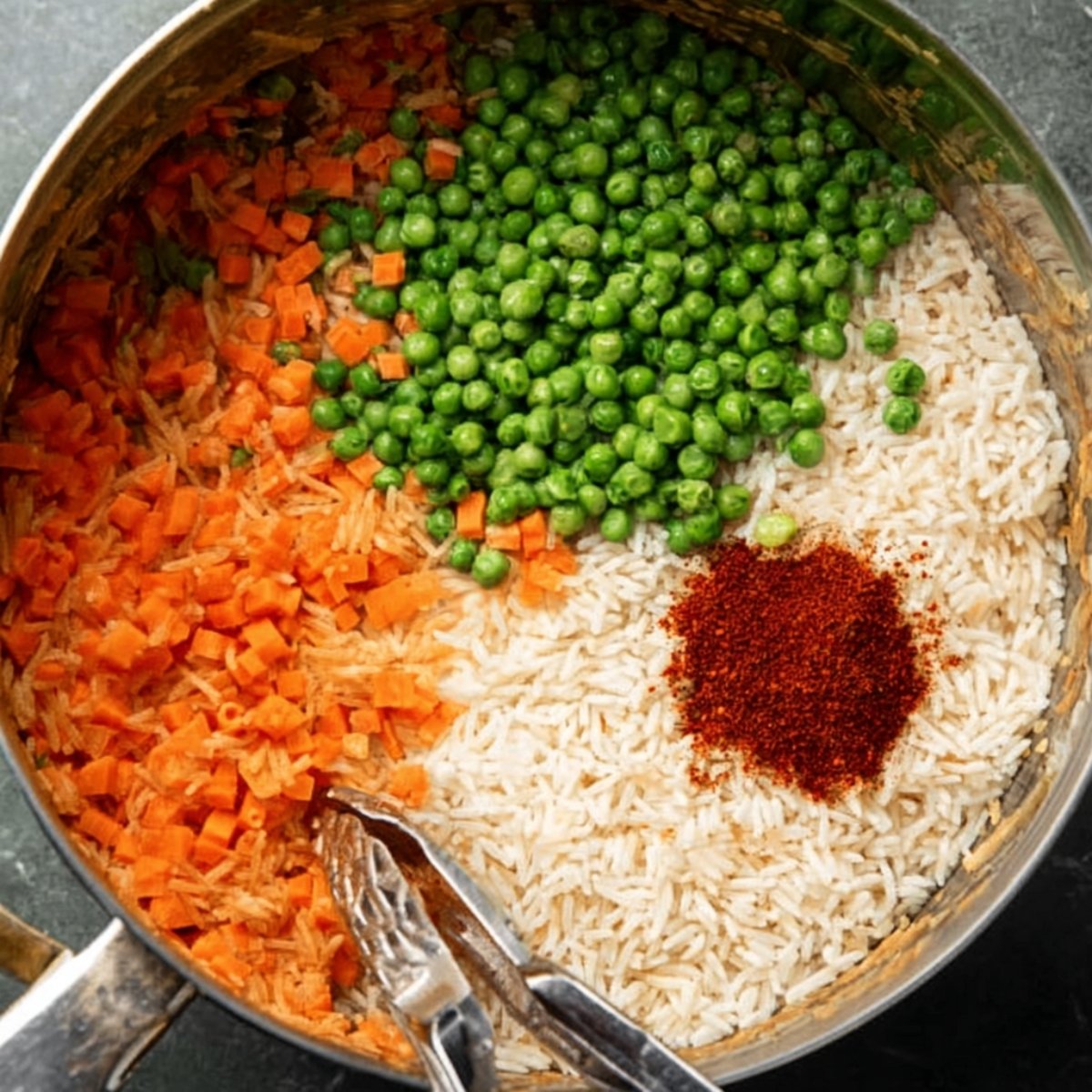 A pot with uncooked rice, diced carrots, green peas, and a small pile of red seasoning, ready to be cooked.