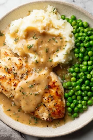 Plate of Boursin chicken served with mashed potatoes topped with gravy and a side of bright green peas