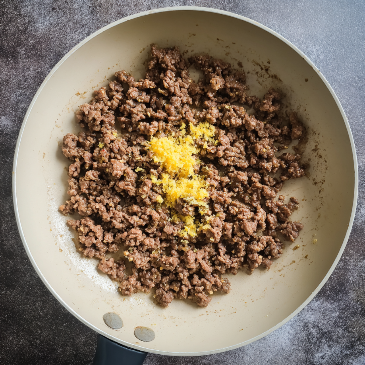 Ground beef being cooked in a nonstick skillet with grated lemon zest sprinkled over the top.